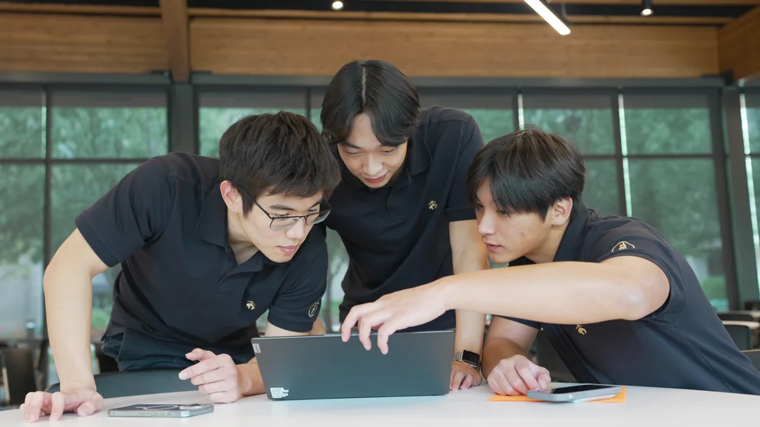 Three Hacktech teammates working together around a laptop